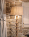 Bamboo look wooden floor lamp with linen shade against stone wall.