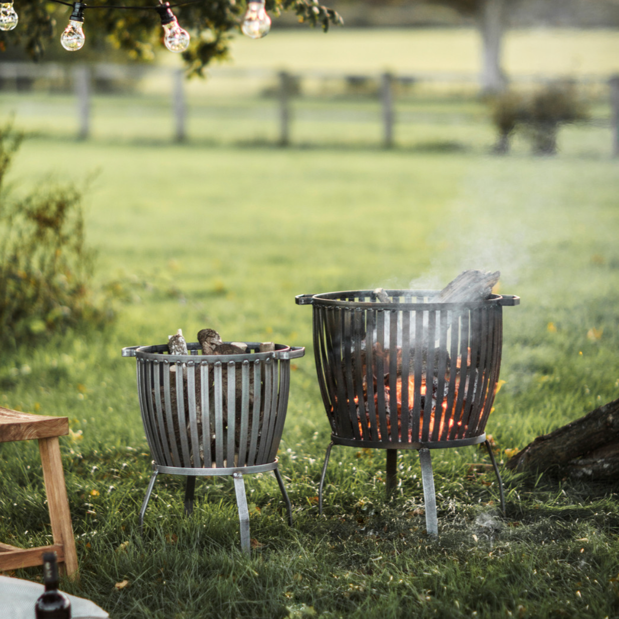 Set of two basket fire pits on lawn.