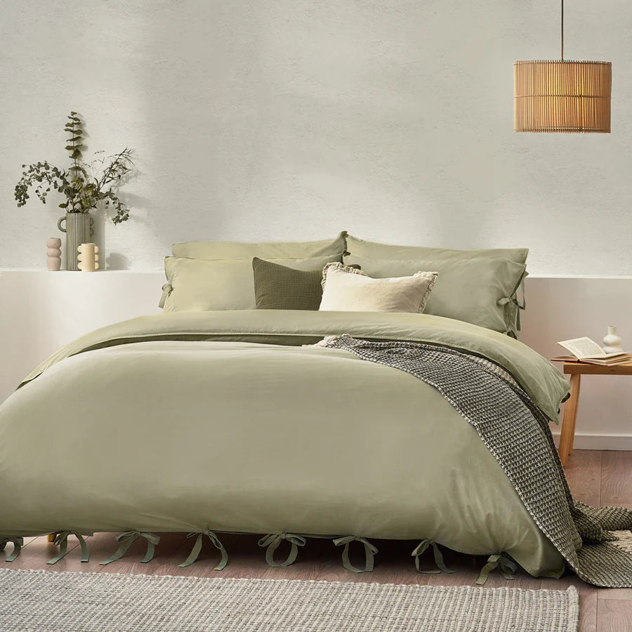 Sage green bedding set with bows, on bed with neutral throw and cushions, bedside styled with bedside table.