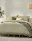 Sage green bedding set with bows, on bed with neutral throw and cushions, bedside styled with bedside table.