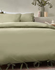 Close up of sage green bedding set with bows, on bed with neutral throw and cushions.