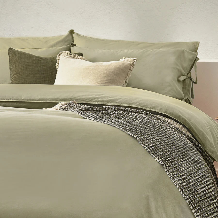 Close up of sage green bedding set with bows, on bed with neutral throw and cushions.