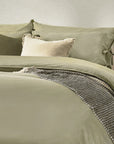 Close up of sage green bedding set with bows, on bed with neutral throw and cushions.