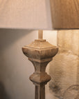 Carved wooden floor lamp with white linen shade in room with stone wall.