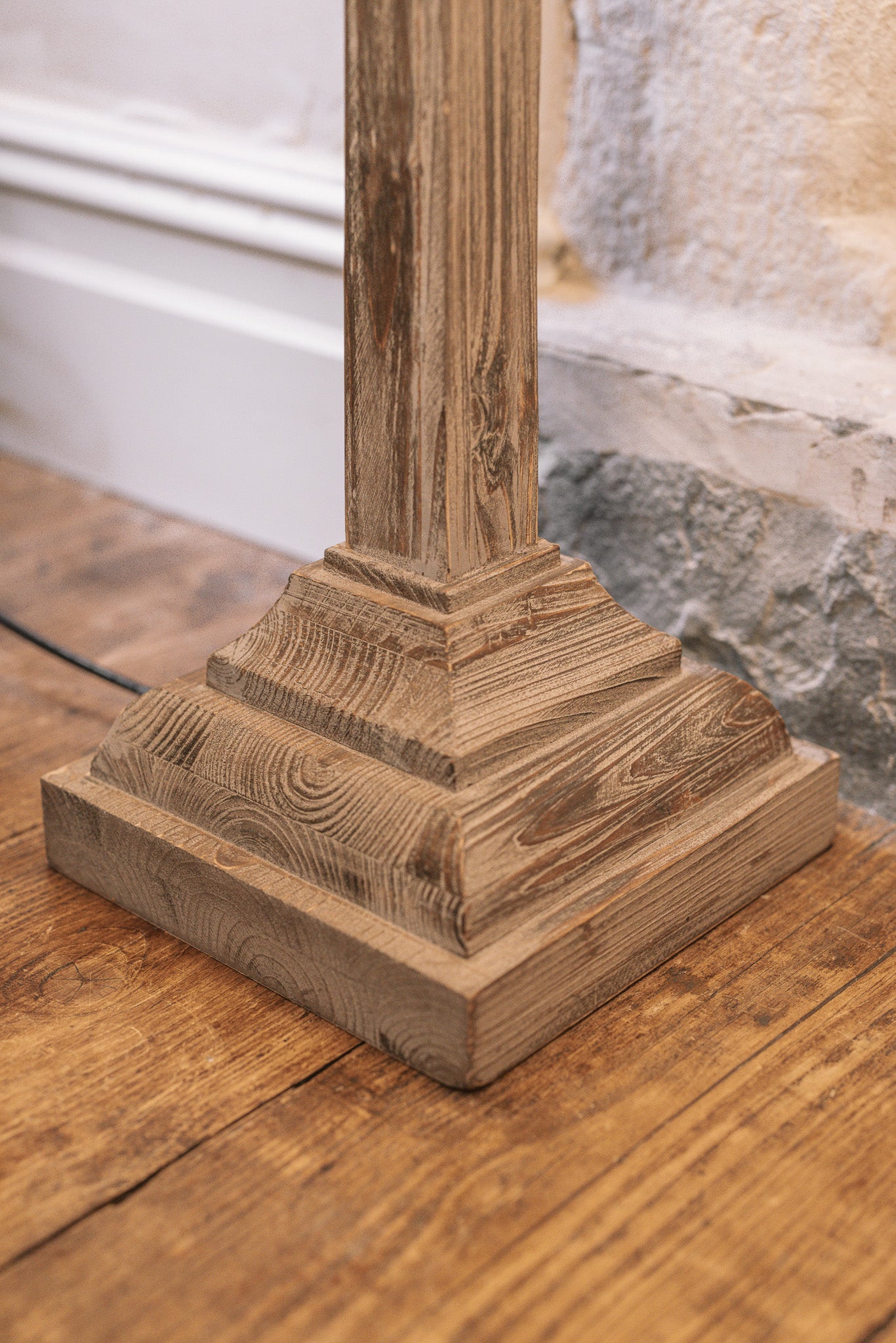 Close up of white washed wooden floor lamp base on wooden floor.