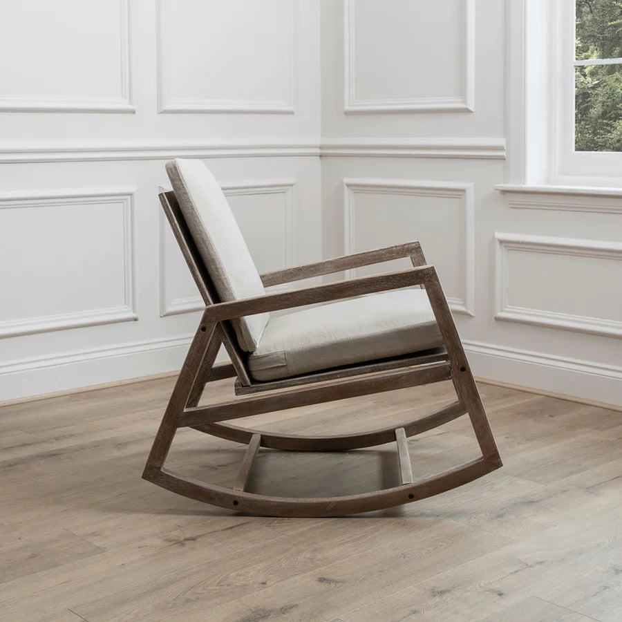 Mango wood rocking chair with natural plush cushions from the side view, in the corner of an empty room.