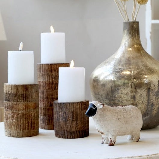Painted sheep ornament on white coffee table with candles and vase. 
