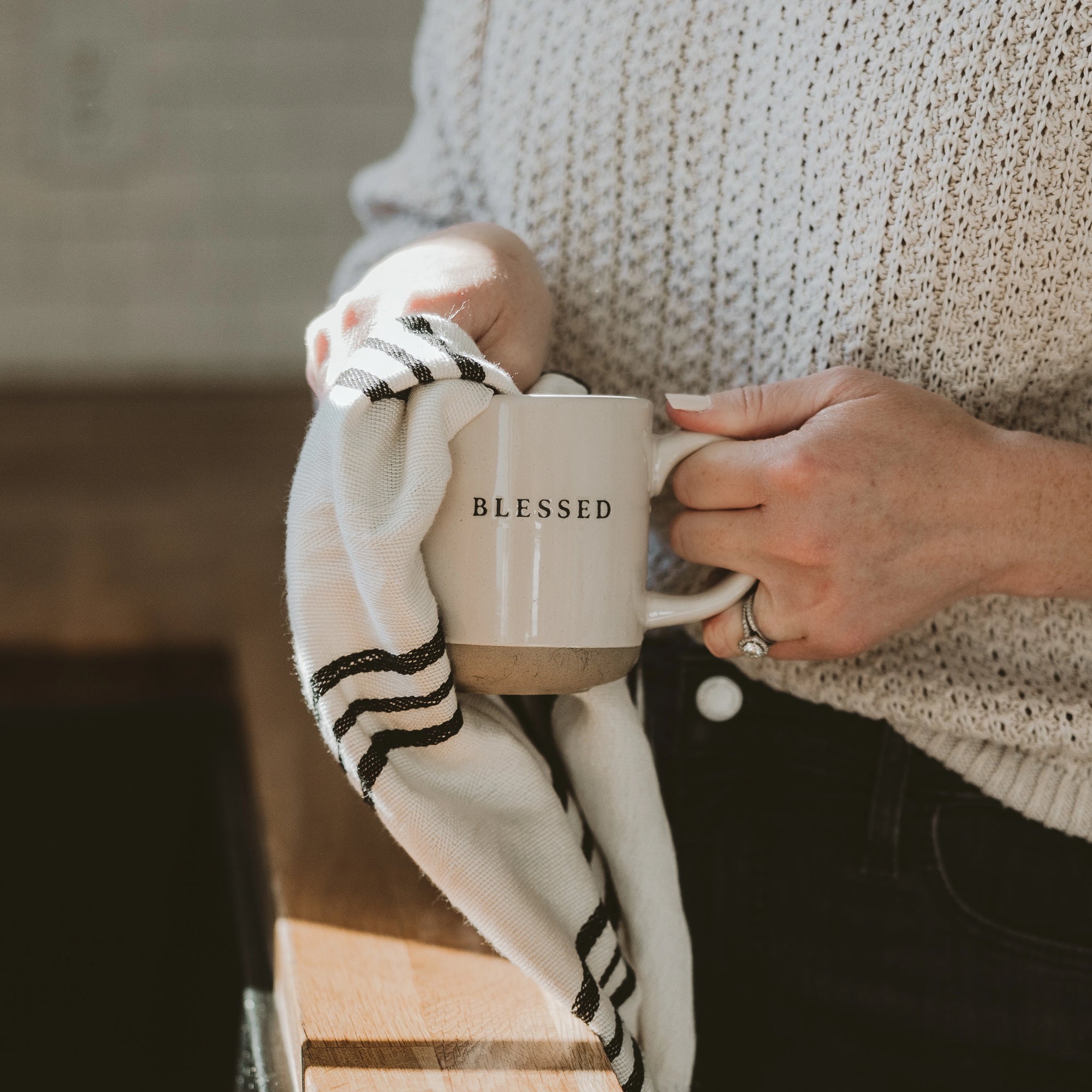 White and neutral brown stoneware mug with 'blessed' written in black text, being dried with tea towel.