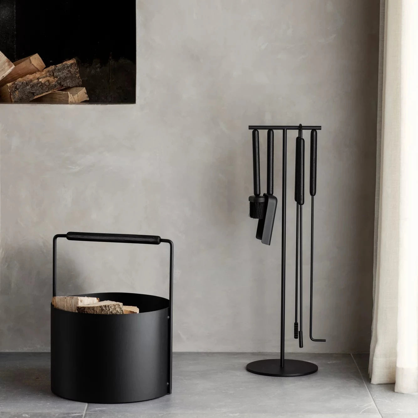 Blomus black 5 piece companion set with black log carrier next to it in front of grey wall.