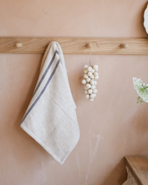 Blue striped kitchen towel hanging on wooden hook on wall.