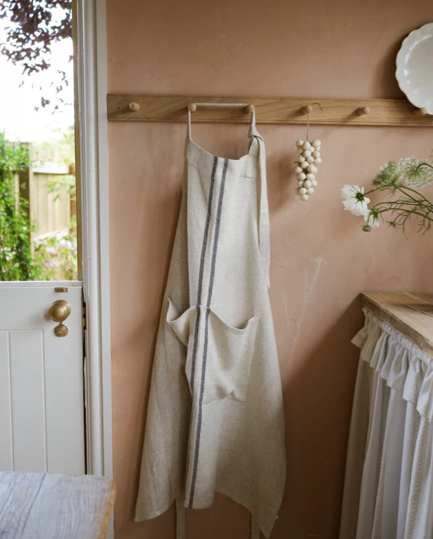 Cream and blue striped linen apron on wooden hook on wall.