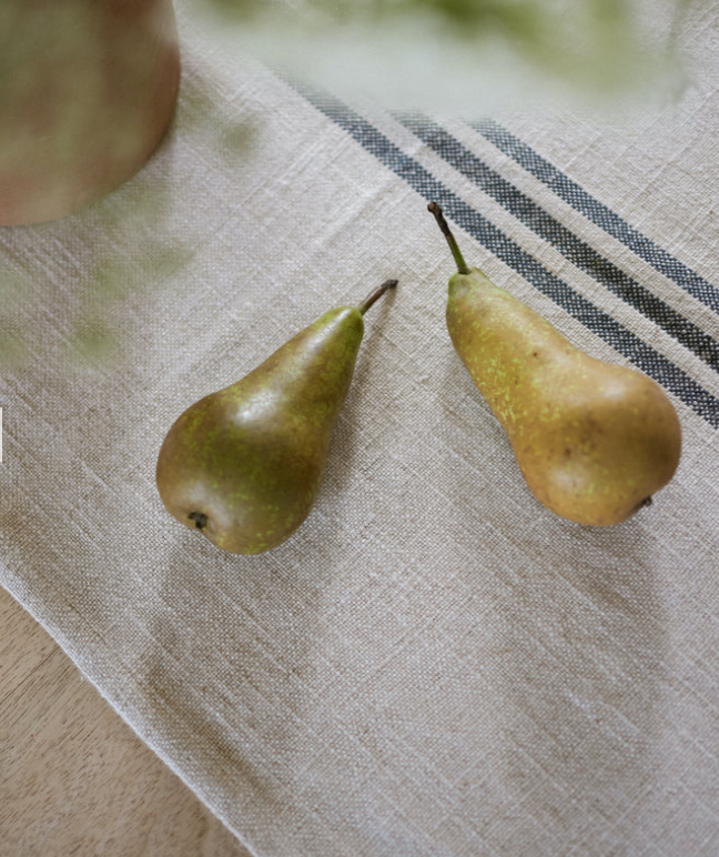 Close up of cream and blue striped linen table runner with two pears on top.