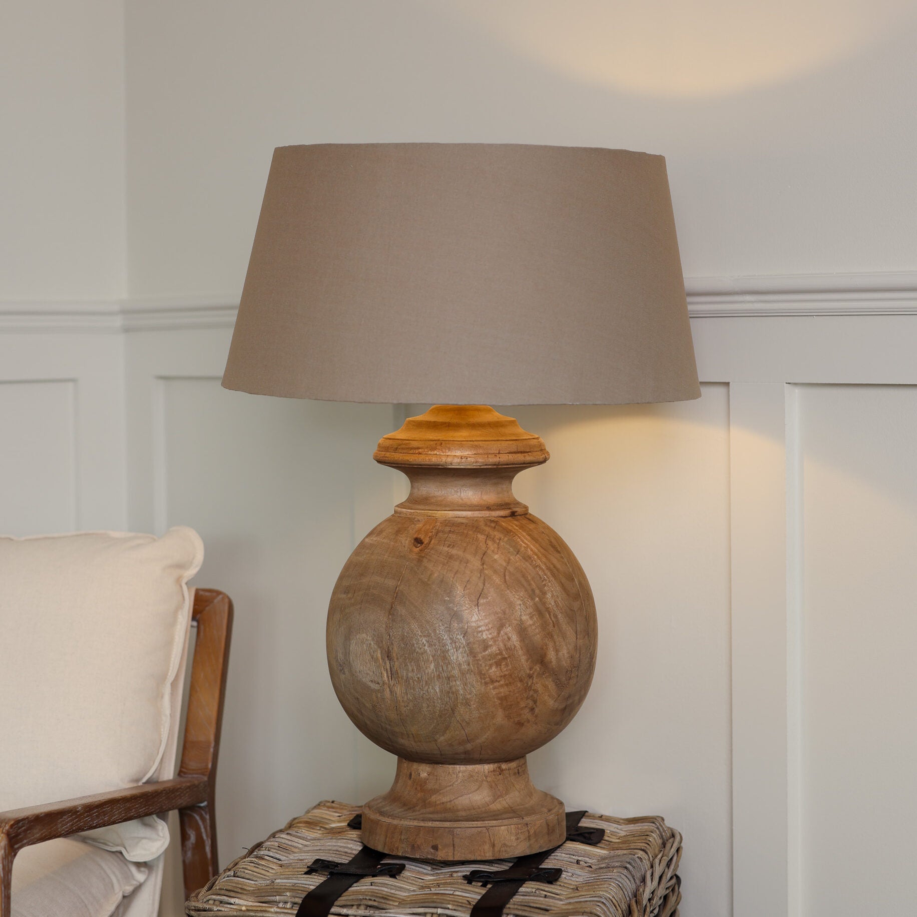 Large round wooden lamp with beige linen shade, on woven side table.