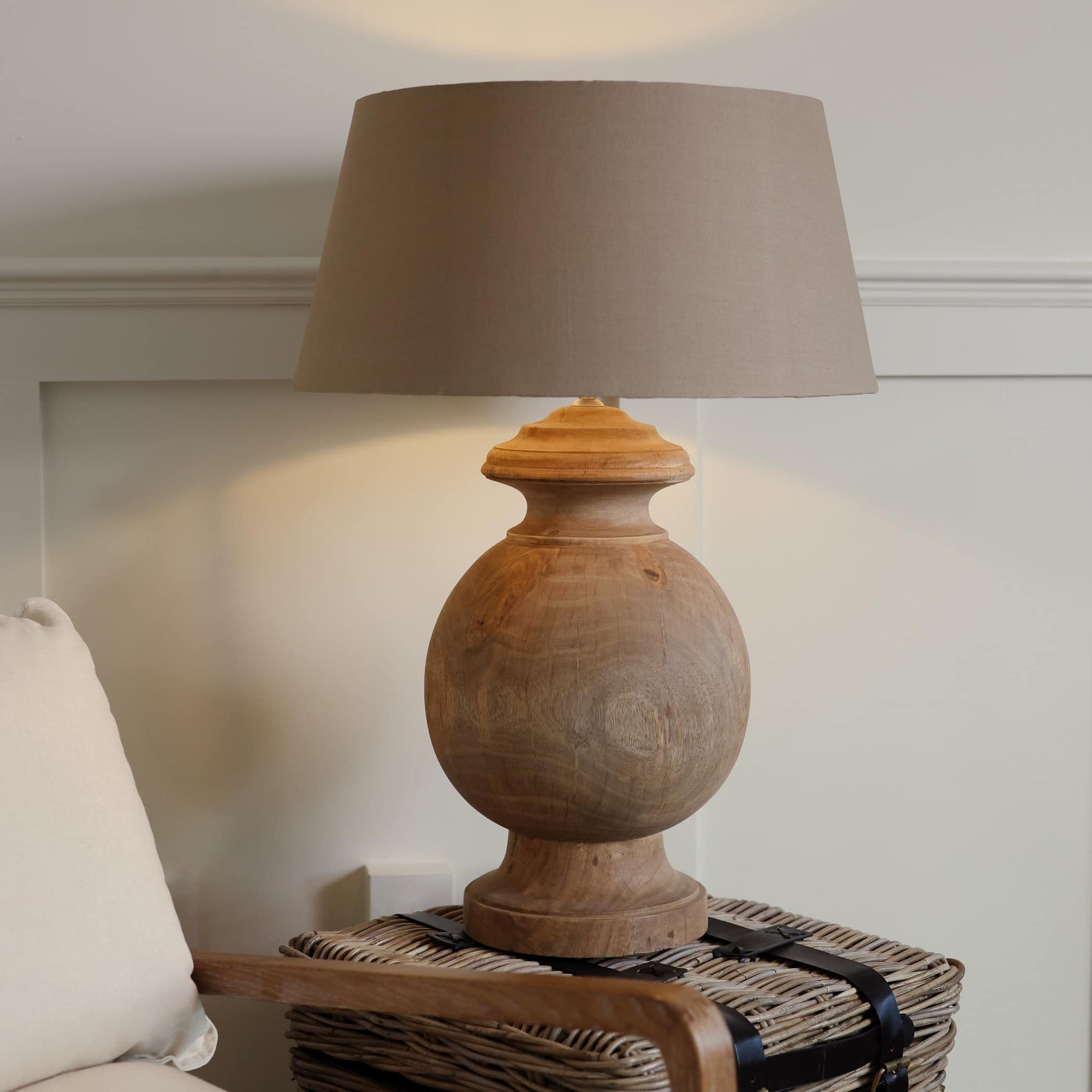 Large round wooden lamp with beige linen shade switched on, on woven side table.
