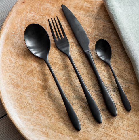 Black cutlery set with fork, knife, spoon and tea spoon on wooden table.