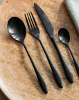 Black cutlery set with fork, knife, spoon and tea spoon on wooden table.