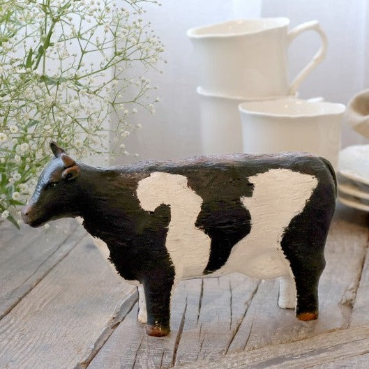 Painted cow ornament on wooden console with white mugs.