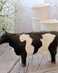 Painted cow ornament on wooden console with white mugs.