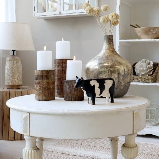 Painted cow ornament on white coffee table with candles and vase. 