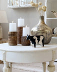 Painted cow ornament on white coffee table with candles and vase. 