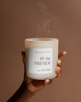 White soy candle held up in one hand, blown out with smoke rising.