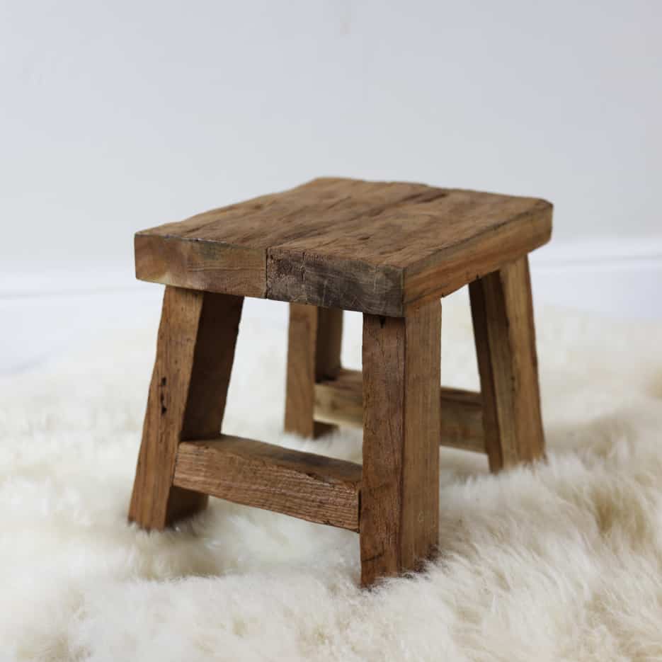 Small wooden stool from side view on white fluffy rug.