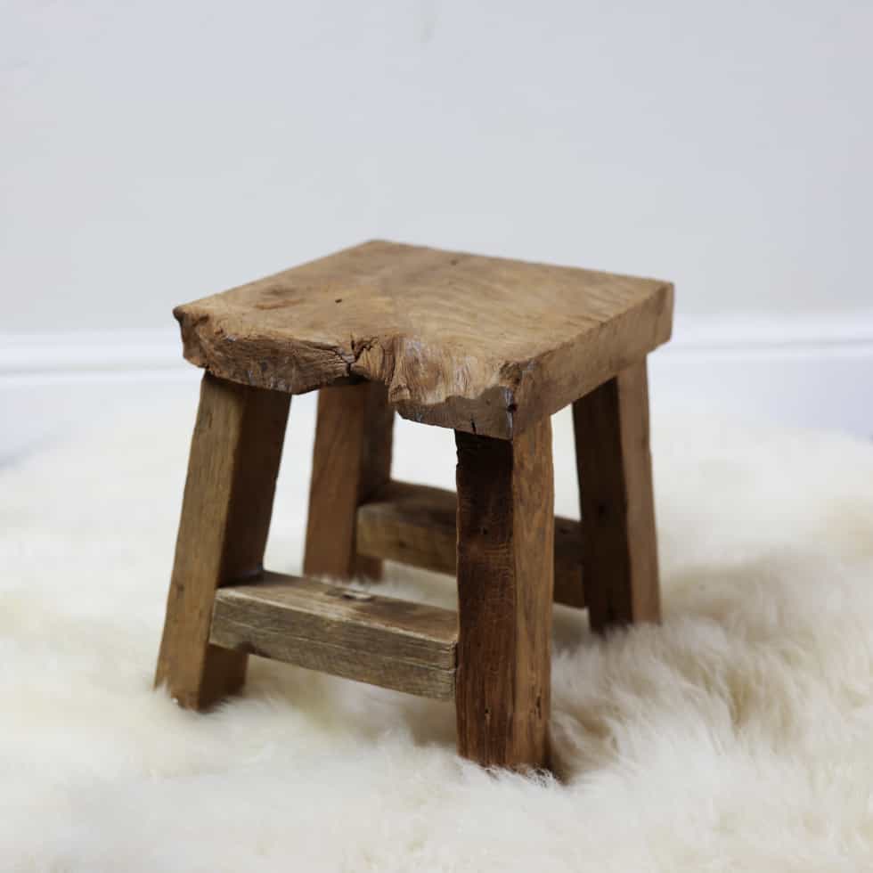 Patina finish small wooden stool on white fluffy rug.