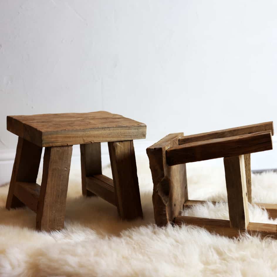 Two small reclaimed wooden stools on white furry rug. One standing and one on the side.