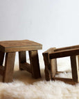 Two small reclaimed wooden stools on white furry rug. One standing and one on the side.
