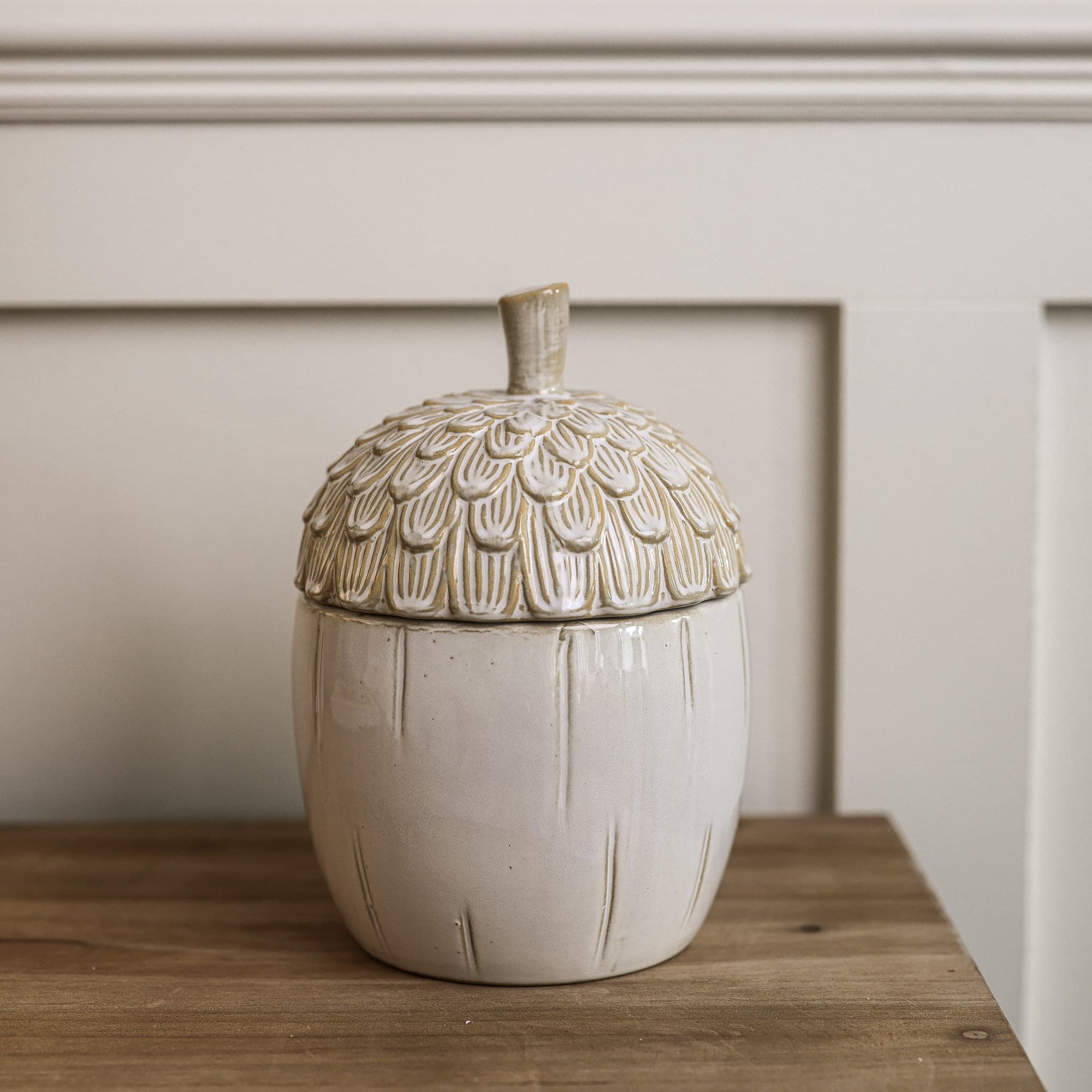 Ceramic off white acorn jar on wooden console table.