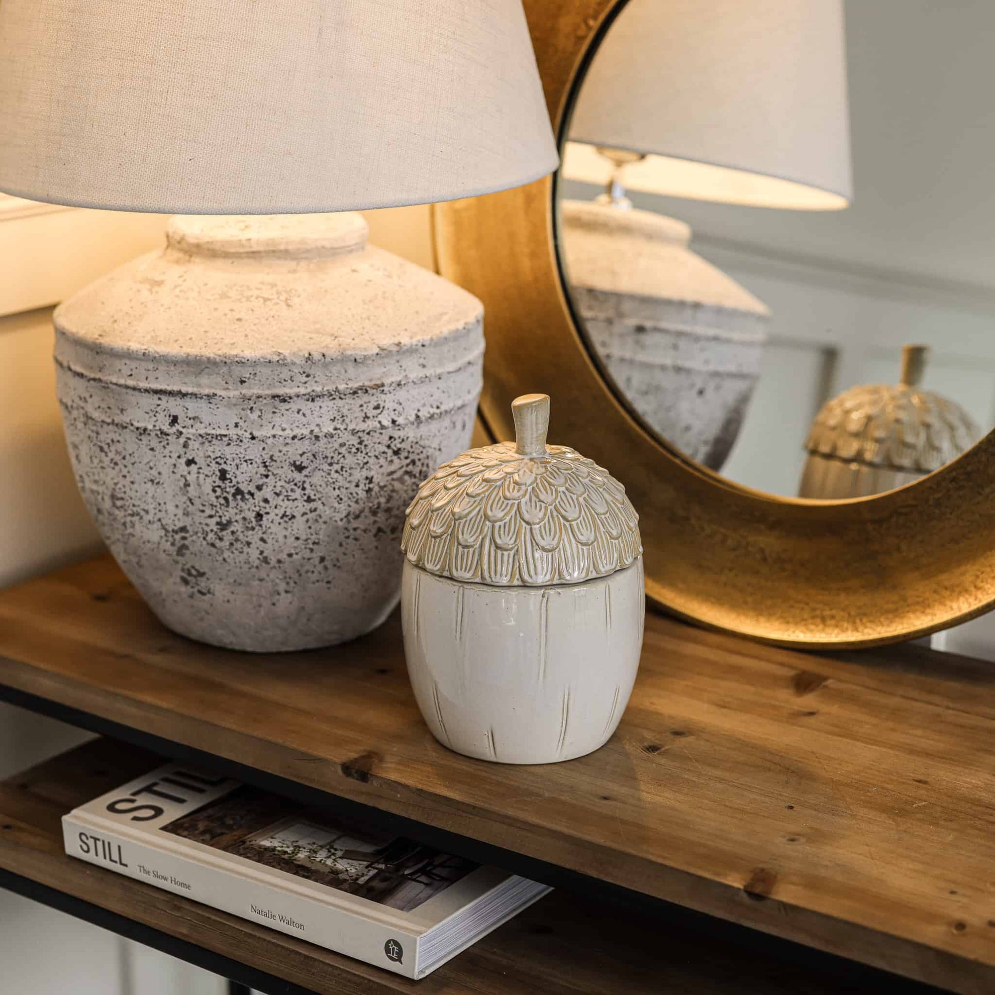 Ceramic acorn storage jar on wooden console with lamp and mirror.