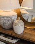 Ceramic acorn storage jar on wooden console with lamp and mirror.