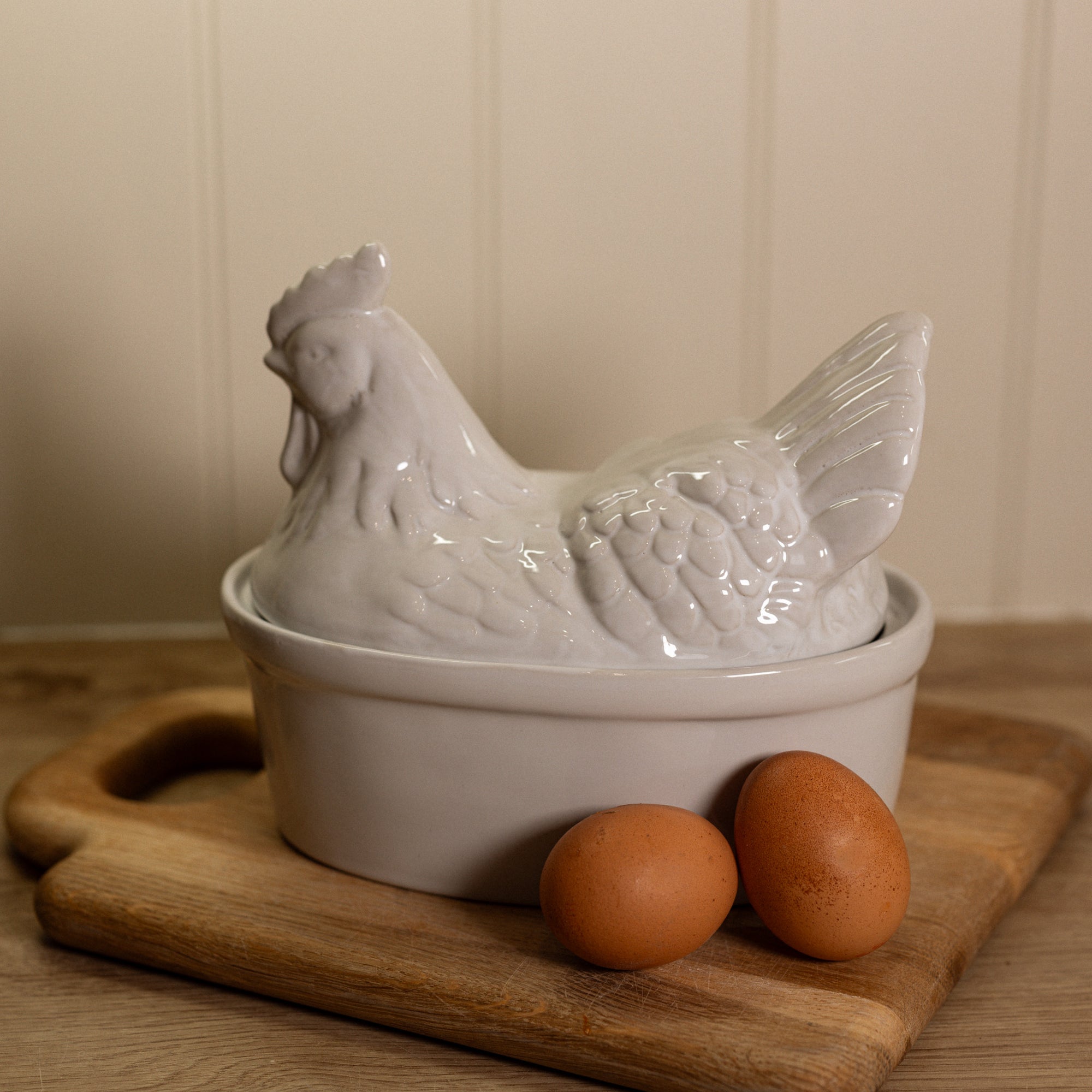 White Ceramic Egg Holder shades like a chicken with two eggs on a wooden chopping board.