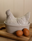 White Ceramic Egg Holder shades like a chicken with two eggs on a wooden chopping board.