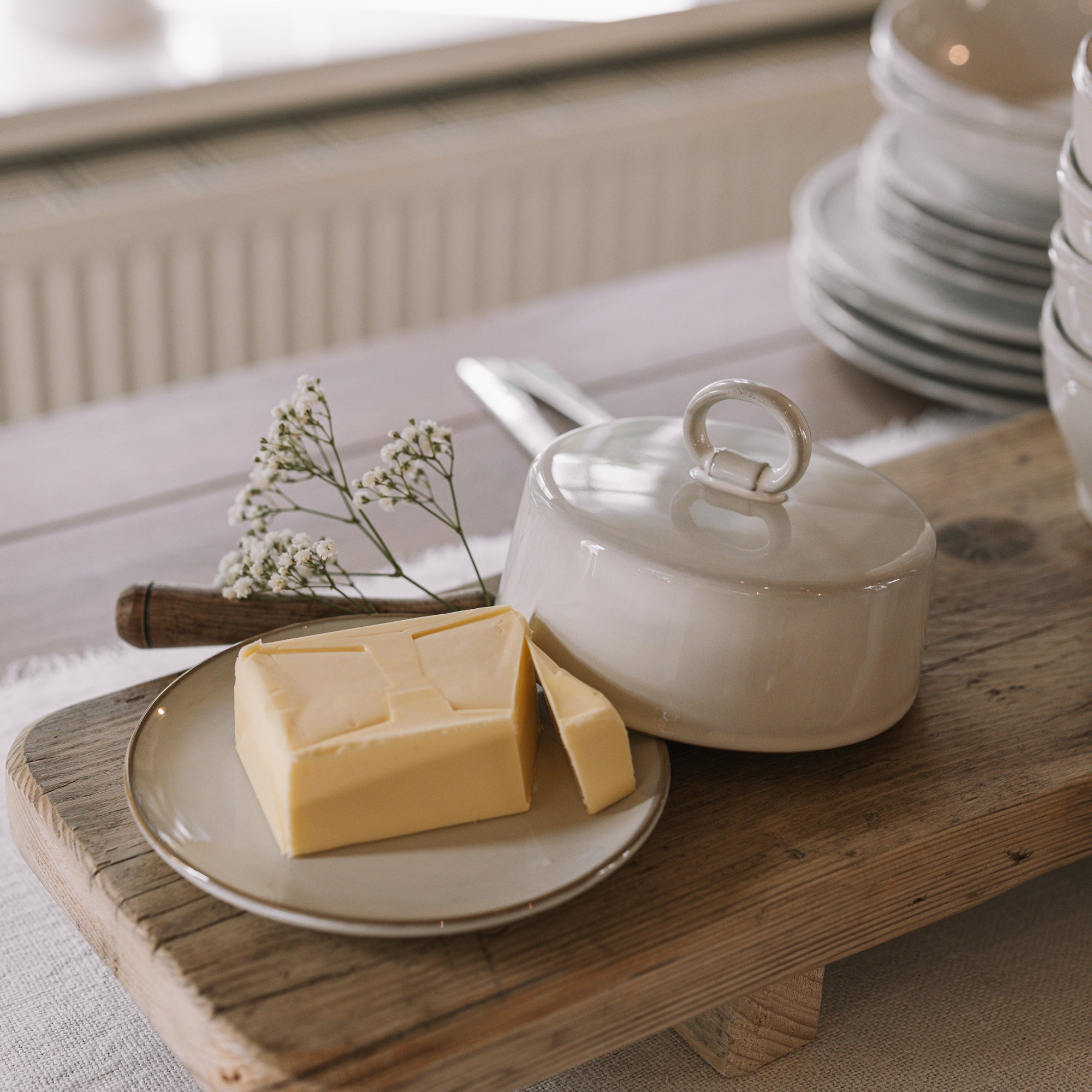 Off white butter dish with lid and loop to open on neutral wooden table with white table cloth.