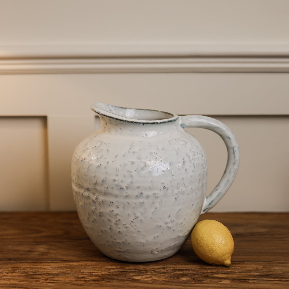 Small speckled glazed ceramic jug on wooden console with lemon.