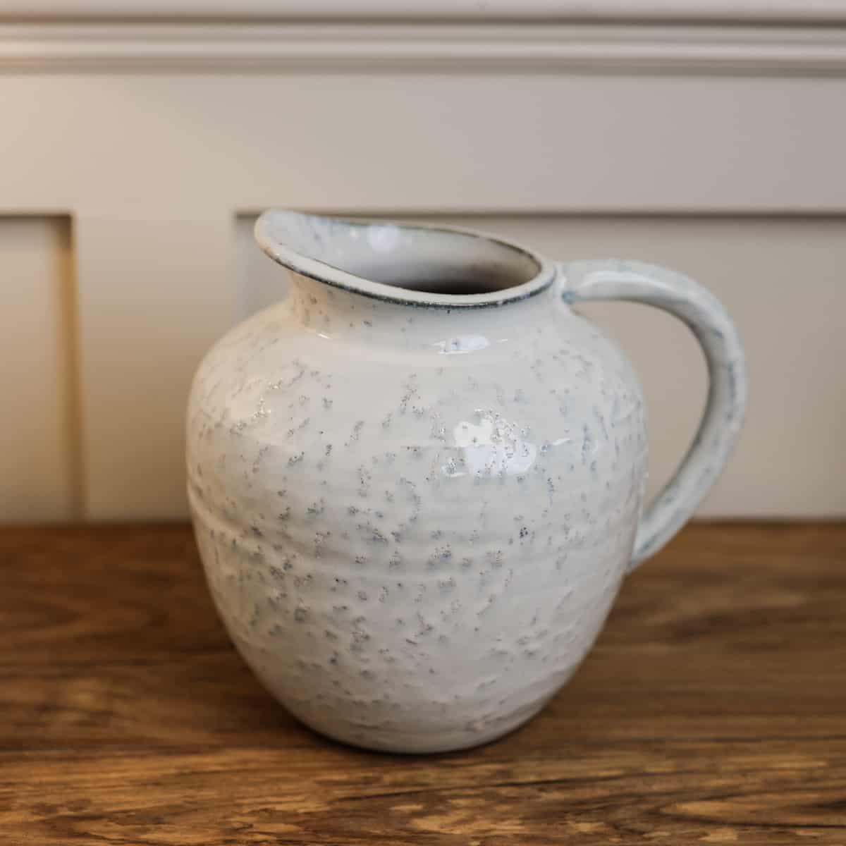 Small white ceramic jug from side on wooden table.