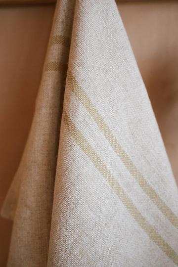 Close up of cream striped kitchen towel hanging from a wooden hook.