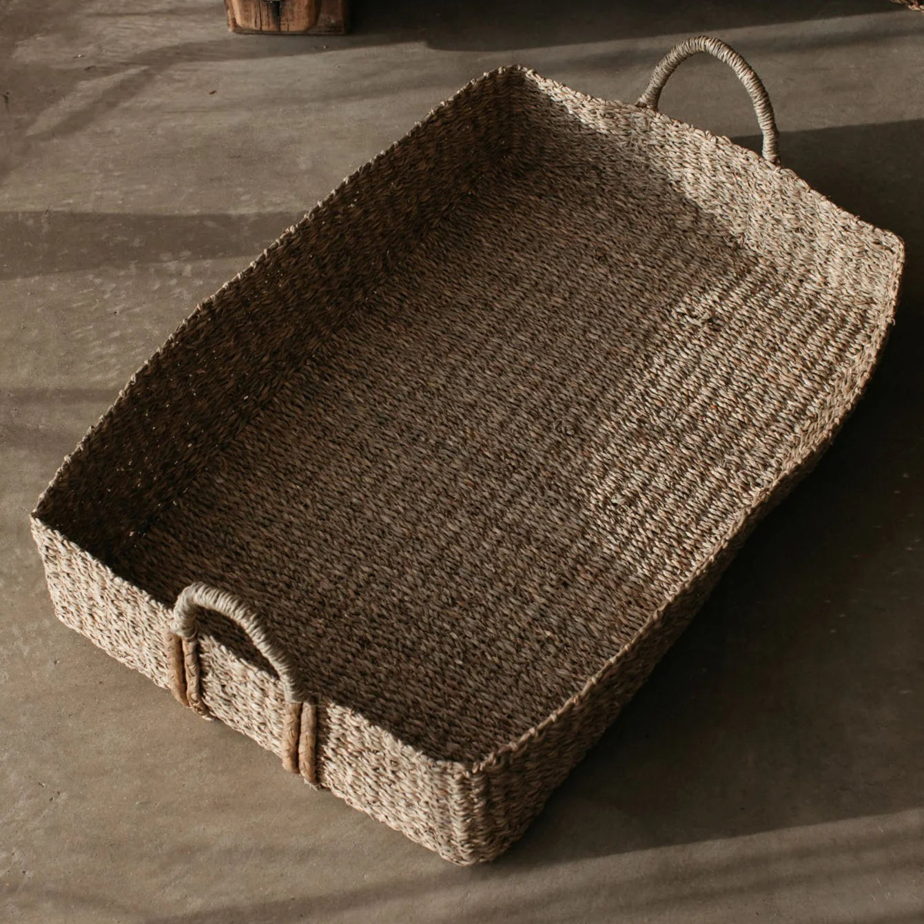 The large Eliza Rectangular Seagrass Basket on a concrete floor.