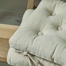 2 light beige seat pads, piled up on wooden bench.