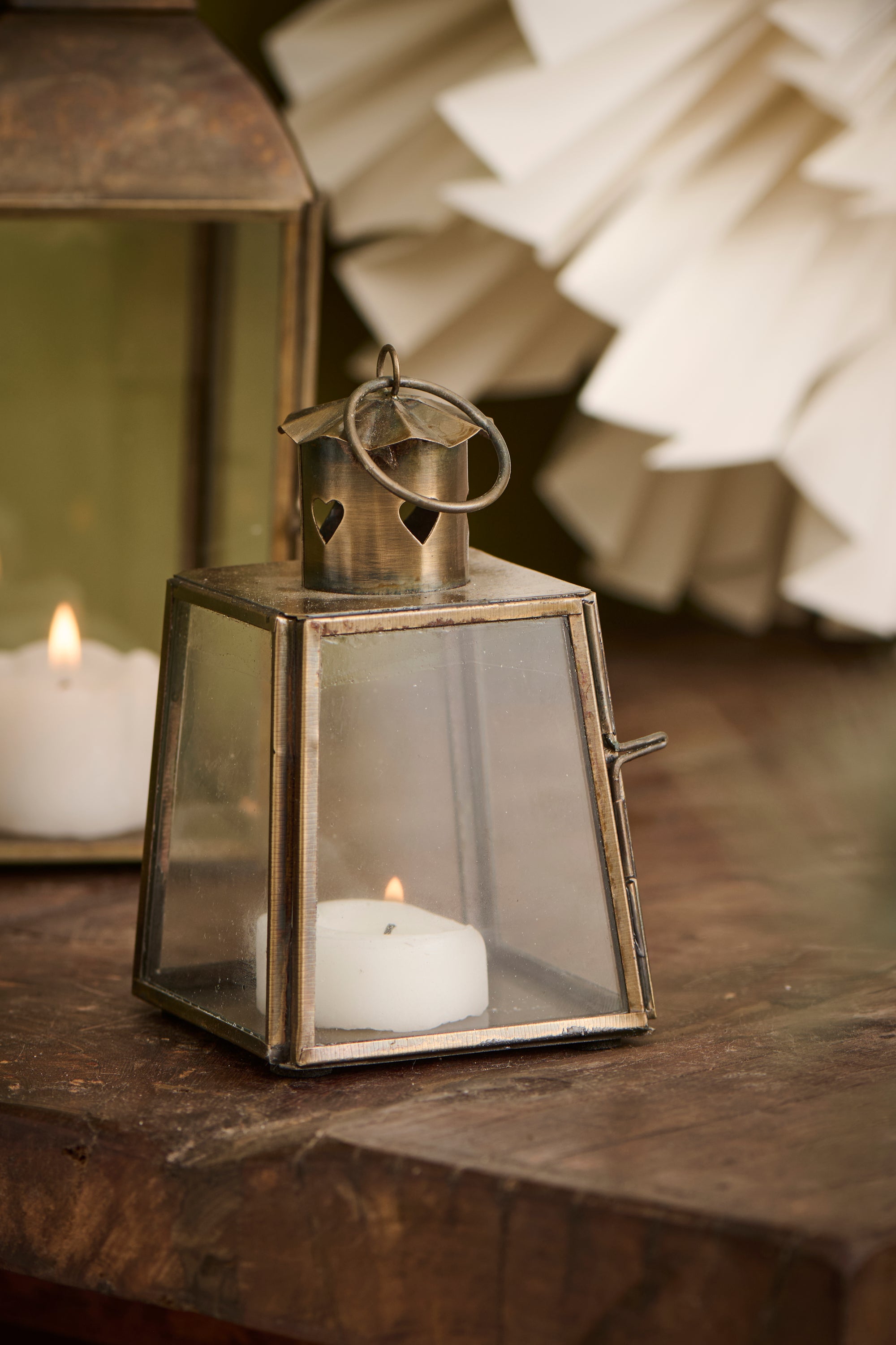 Mini bronze tealight candle lantern on wooden table, with lit candle inside.