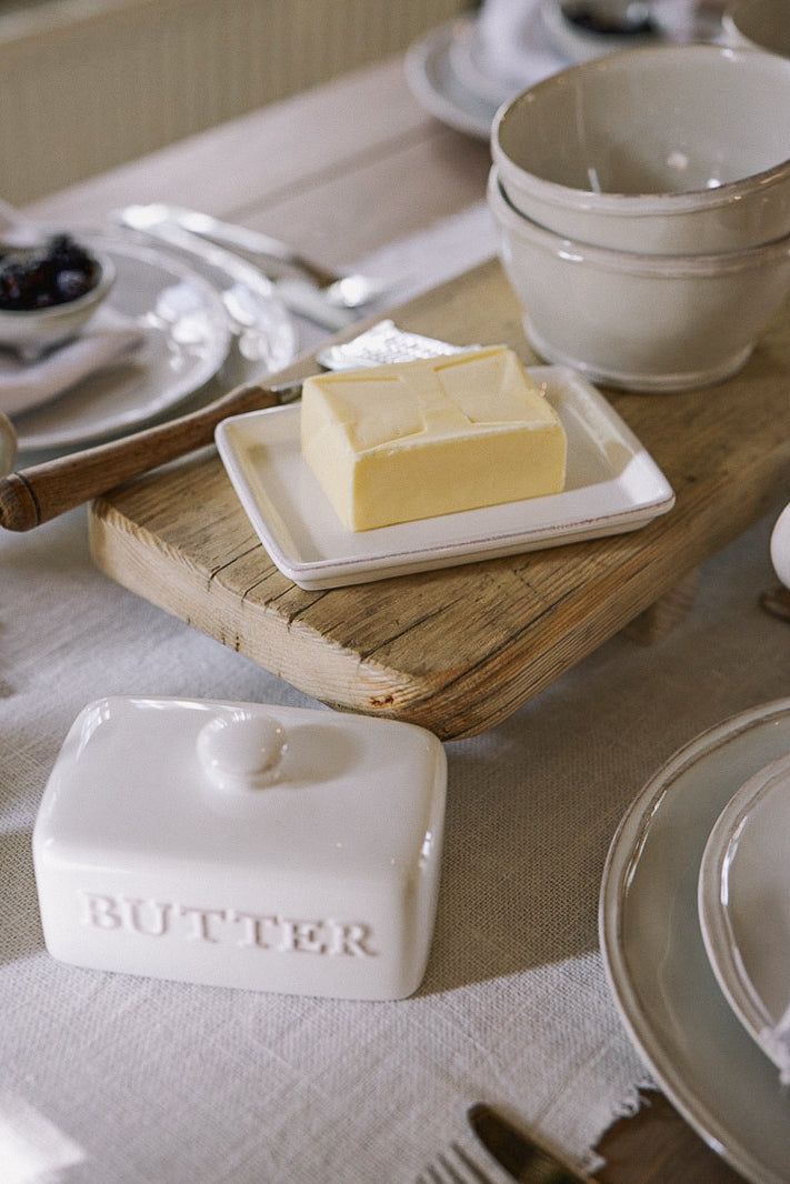 Ceramic butter dish with embossed 'butter' name, and block of butter on wooden serving board.