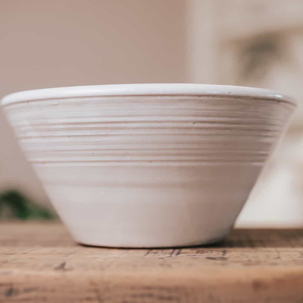 White ceramic bowl with ridges on wooden console. 