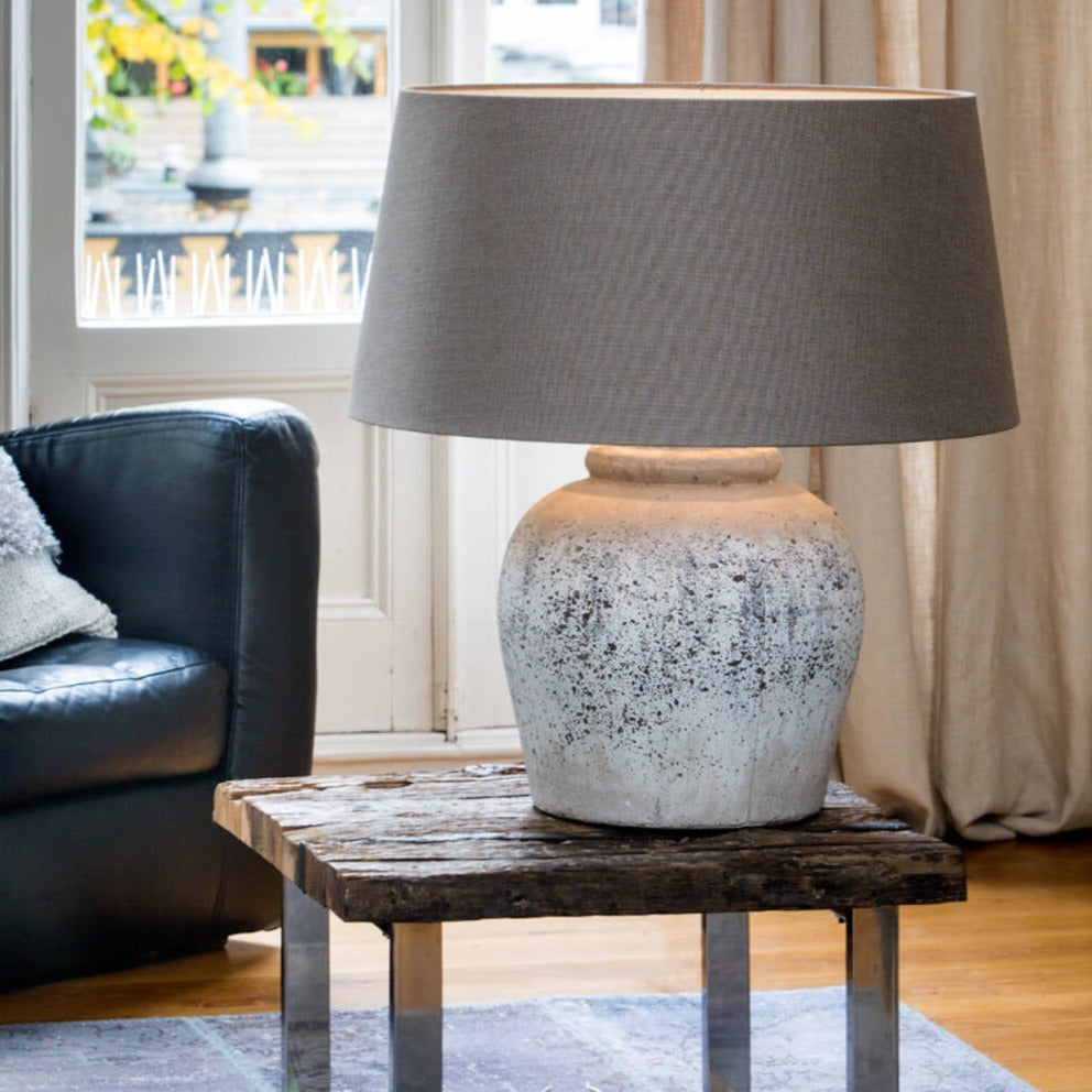 Large antique grey lamp base with grey shade on wooden table.