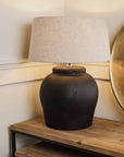 Matte black lamp with neutral shade, switched on on wooden console