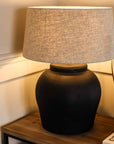 Close up of matte black lamp with neutral shade, switched on on wooden console.