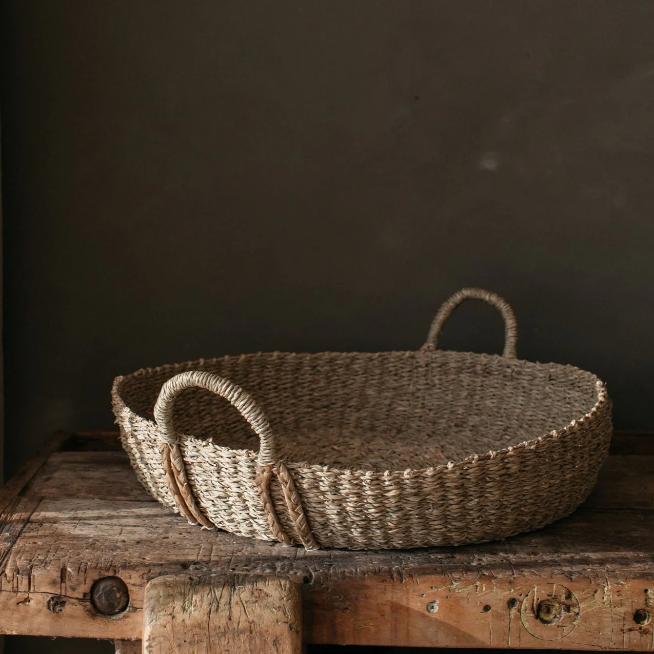 The large Evelyn Seagrass Basket on a chunky wooden table against a brown wall.