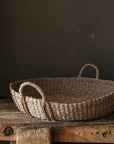 The large Evelyn Seagrass Basket on a chunky wooden table against a brown wall.