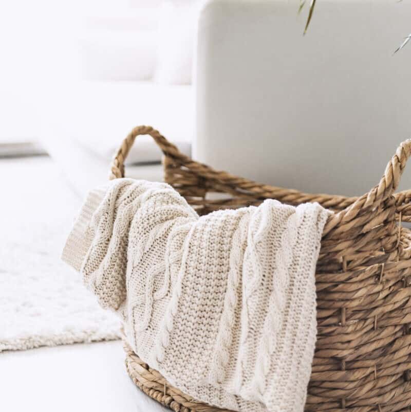 Cream knitted throw hanging over a woven wicker basket.