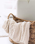 Cream knitted throw hanging over a woven wicker basket.